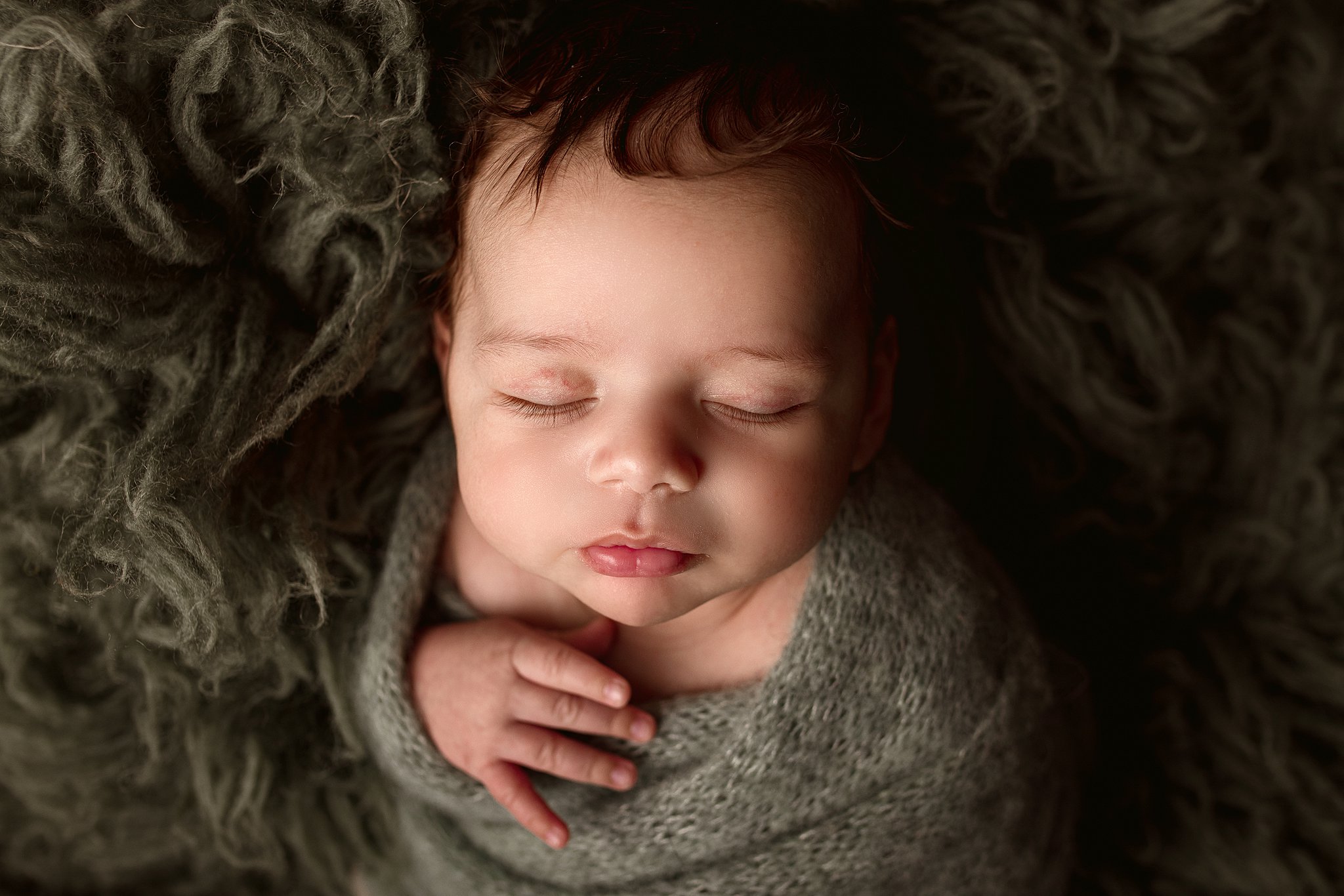 A newborn baby sleeps with one hand out of its swaddle on a furry blanket best pediatrician toronoto