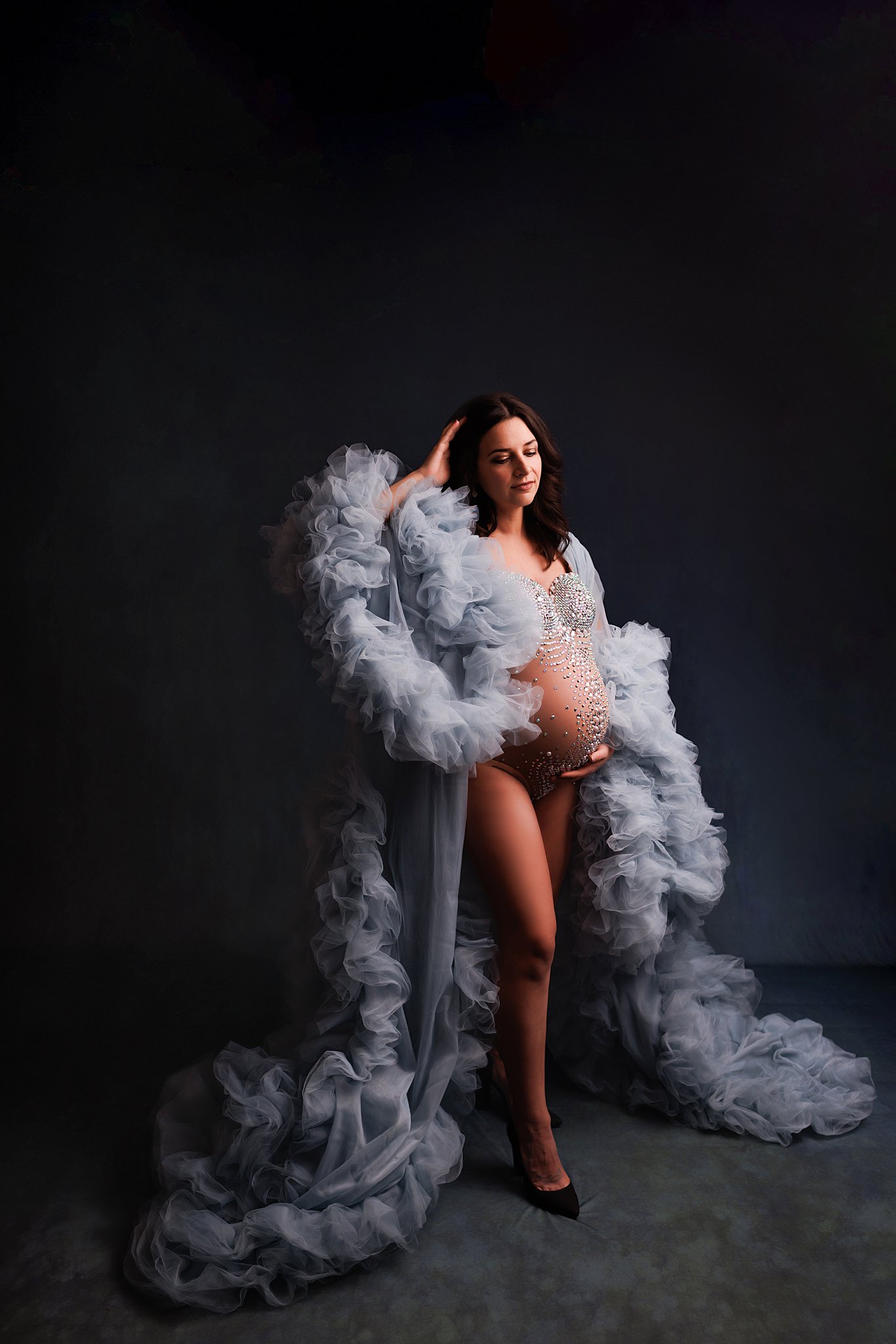 A mother to be in a blue tule luxury maternity gown stands in a studio running a hand through her hair bradford ultrasound