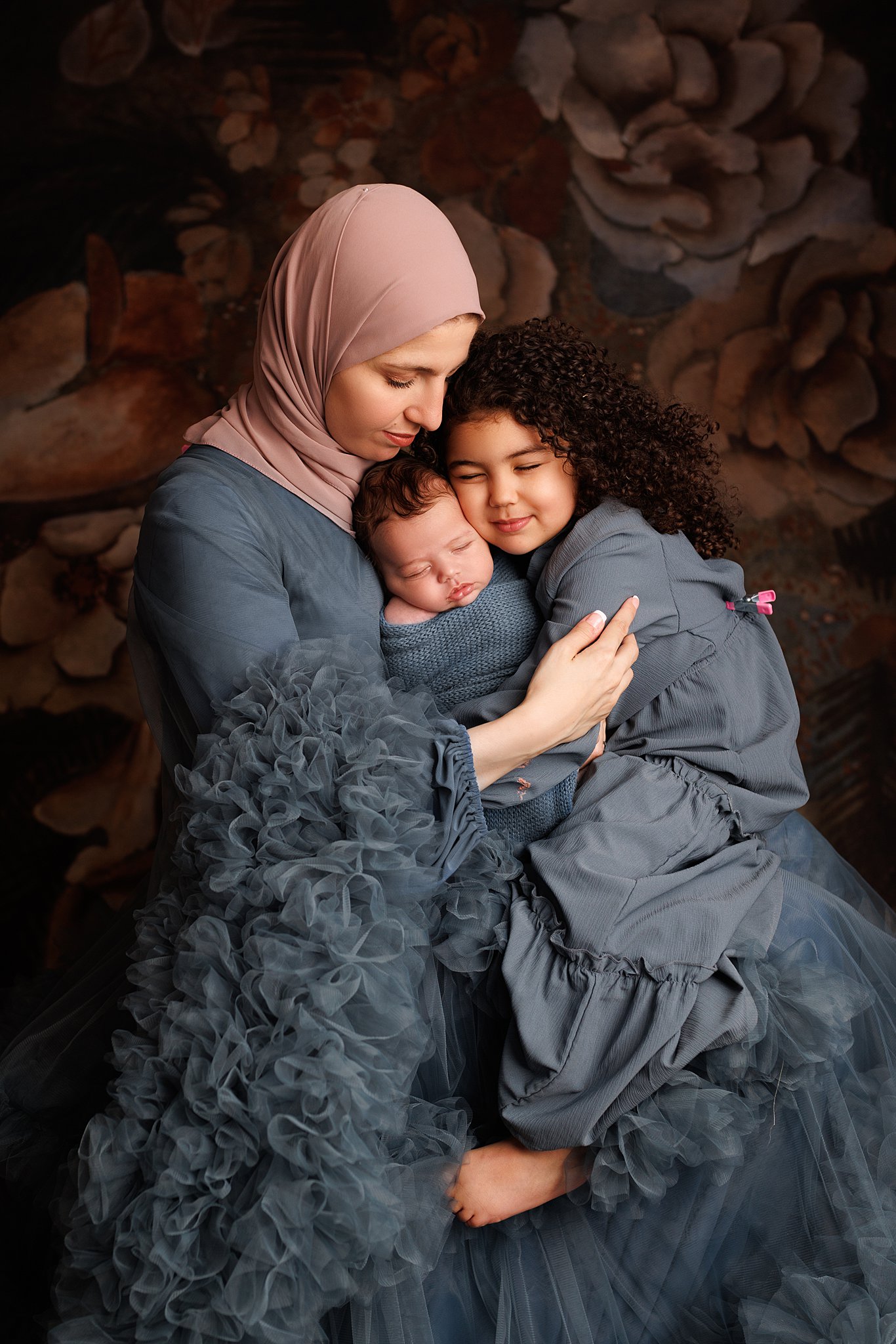 A mother cuddles with her newborn baby and young daughter in her lap love me do baby