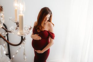 Beautiful pregnant woman in red dress posing for maternity session.