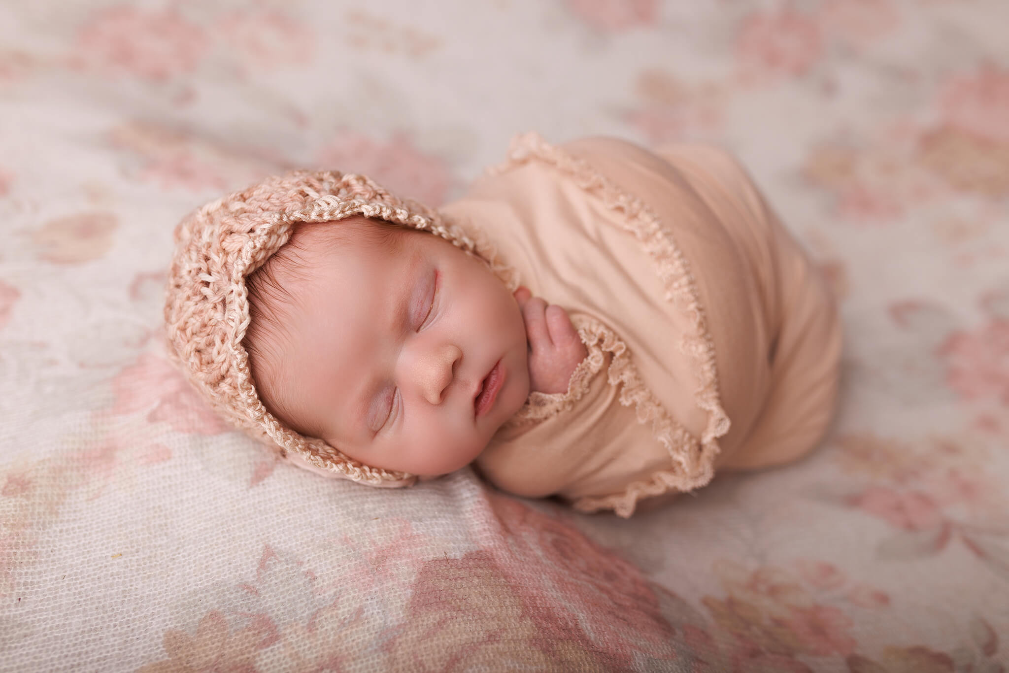 A newborn baby sleeps wrapped in a pink swaddle and matching knit bonnet new life midwives