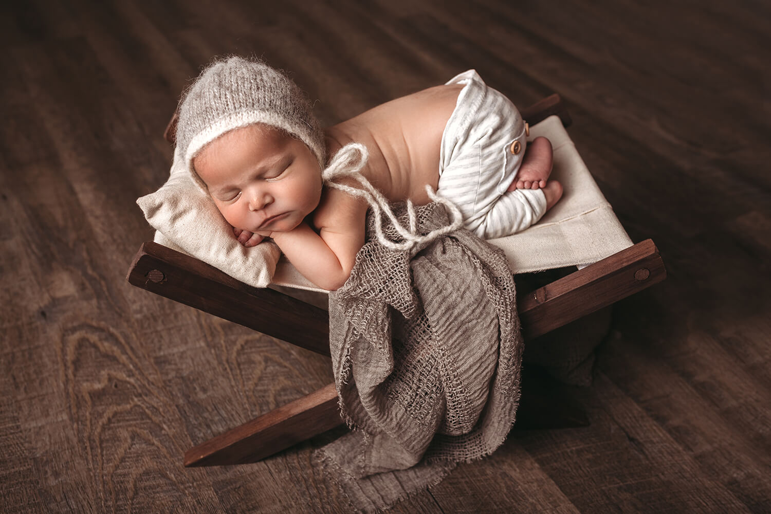 Photo of baby sleeping on a chair with blanket and bonnet.