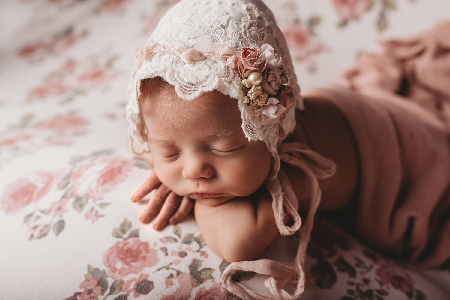 Studio photo of a newborn on a bed wearing a bonnet. You Name It Baby
