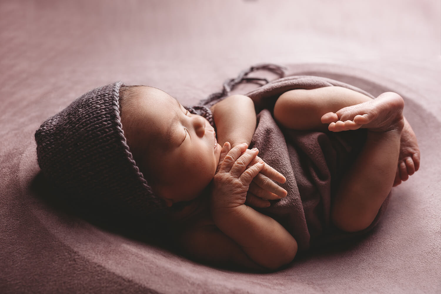 Photo of baby curled up in a blanket and knit hat.