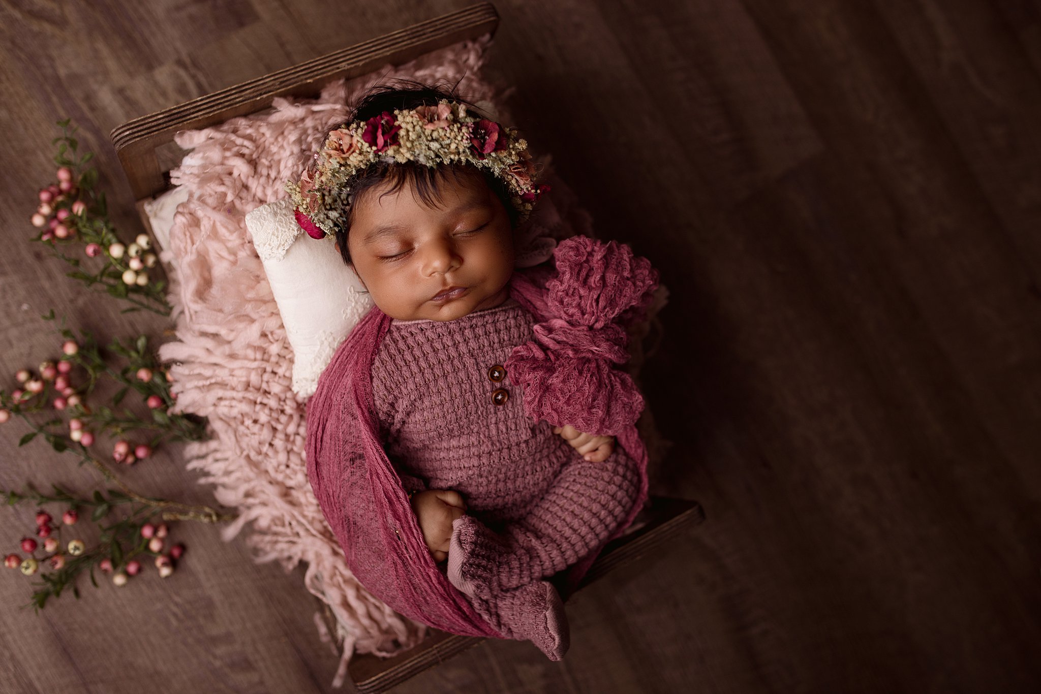 A newborn baby in a purple knit onesie sleeps in a tiny wooden bed peach boy toronto