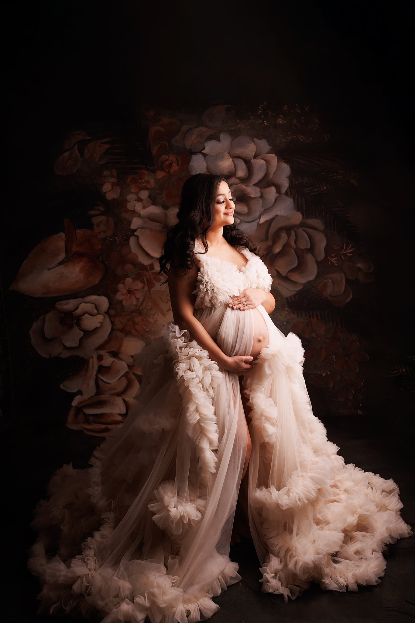 A mother to be stands in a studio wearing a fluffy maternity gown with bump exposed prenatal yoga toronto